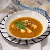 Un plato de sopa de pescado con trozos de marisco, gambas y mejillones, decorado con perejil fresco.