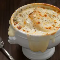Sopa de cebolla gratinada, con queso derretido y hierbas, humeante y deliciosa, lista para ser disfrutada con una cuchara.