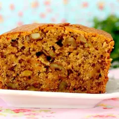 Un delicioso bizcocho de zanahoria, con trozos de nueces y un color dorado apetitoso, servido en un plato blanco sobre un mantel floral.