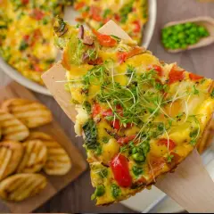 Rebanada de frittata de verduras con guisantes, pimientos y brotes frescos, servida con patatas a la parrilla.
