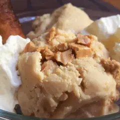 Delicioso helado de turrón con trozos crujientes, acompañado de nata montada y un bizcocho dorado.