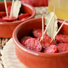 Dos cuencos de barro con chorizos a la sidra, decorados con palillos y hojas de laurel.