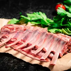 Costillar de cordero crudo, listo para preparar un delicioso cordero al chilindrón con perejil y tomates.