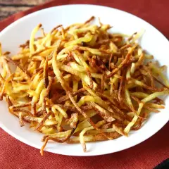 Un plato blanco lleno de crujientes patatas paja doradas, listas para ser disfrutadas.