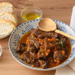 Un reconfortante plato de ternera en salsa, con trozos tiernos de carne, zanahoria y apio, servido con pan y perejil fresco.