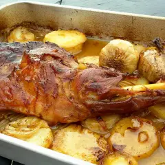 Paletilla de cordero asada con patatas y ajos dorados en una bandeja. Jugosa y apetitosa, lista para servir.