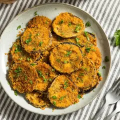 Plato de berenjenas rebozadas, doradas y crujientes, espolvoreadas con perejil fresco.