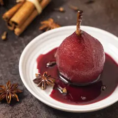 Peras al vino, cocinadas a la perfección, servidas en un plato blanco con especias como anís estrellado y canela.