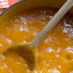 Cuchara de madera removiendo una burbujeante mermelada de melocotón casera en una olla.