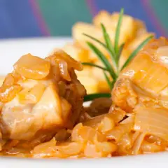Dos trozos de conejo en escabeche, cubiertos de cebolla caramelizada, acompañados de patatas fritas y una ramita de romero.