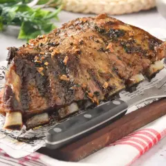 Costillas de churrasco de cerdo glaseadas, servidas sobre papel con texto y acompañadas de un tenedor y cuchillo.