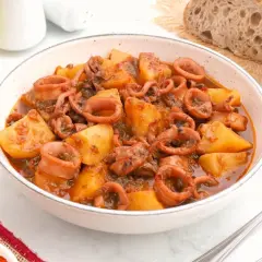 Un tazón de patatas con calamares en salsa, acompañado de pan rústico y un vaso de cerveza.