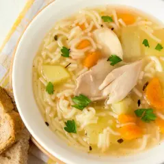 Un reconfortante plato de sopa de pollo receta, con fideos finos, trozos de pollo, patatas y zanahorias, adornado con perejil fresco.