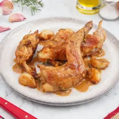 Delicioso conejo al ajillo servido en un plato, con ajos enteros asados y salsa dorada.