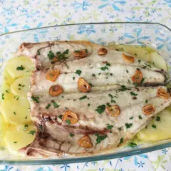 Lubina a la espalda horneada con patatas, ajo y perejil en una fuente de cristal.