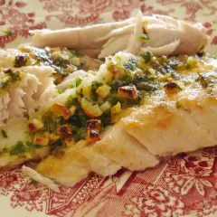 Deliciosa ventresca al horno, jugosa y dorada, con un aderezo verde de hierbas y ajo.