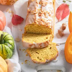 Bizcocho de calabaza, receta de la abuela, con glaseado y almendras. Rodeado de calabazas y hojas de otoño.