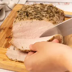 Un jugoso lomo a la sal, recién horneado y cubierto de hierbas, se corta en rodajas tiernas sobre una tabla de madera.