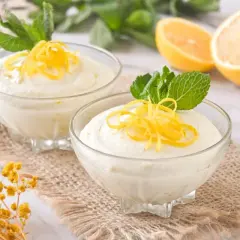 Dos copas de cremoso mousse de limón con leche condensada, decoradas con ralladura de limón y menta.