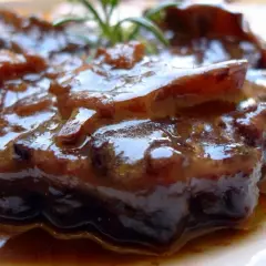 Plato de rabo de toro estofado, con una salsa oscura y brillante, adornado con una ramita de romero.