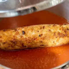 Rollo de bonito casa consuelo, dorado y crujiente, nadando en una salsa de tomate casera en una sartén.
