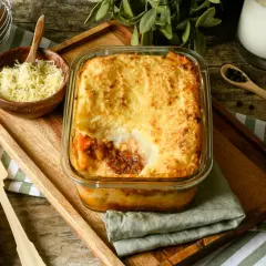 Pastel de carne picada recién horneado, con una capa dorada de puré de patatas y queso gratinado. Se sirve en una fuente de cristal sobre una tabla de madera.