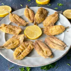 Plato de boquerones fritos crujientes, adornado con rodajas de limón y perejil fresco. Un aperitivo perfecto.