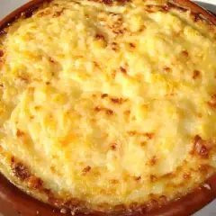 Un delicioso pure de patata gratinado, con bordes dorados y burbujeante, servido en una cazuela de barro.