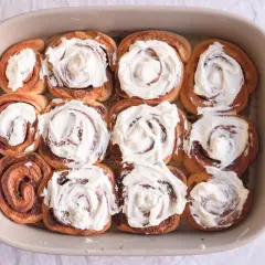 Horneados rollitos de canela cubiertos con glaseado cremoso en un molde de cerámica.