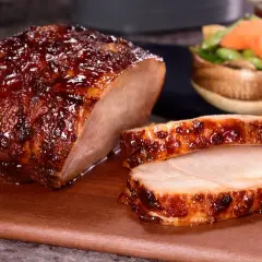 Jugoso lomo adobado glaseado, cortado en rodajas, servido en tabla de madera con guarnición de verduras.