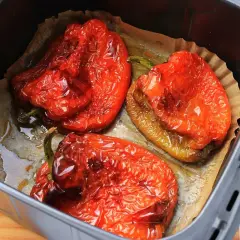 Tres pimientos rojos asados en freidora de aire, con piel arrugada y jugosos, listos para disfrutar.