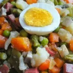 Un plato de menestra de verduras con trozos de zanahoria, guisantes, judías verdes, coliflor y patata, coronado con medio huevo duro.