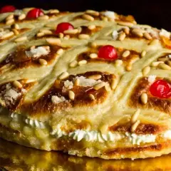 Deliciosa coca de Sant Joan rellena de crema, decorada con piñones, cerezas rojas y azúcar.