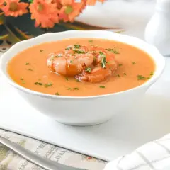 Deliciosa crema de marisco servida en un cuenco blanco, coronada con gambas y perejil picado.