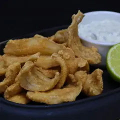 Crujiente bacaladilla frita servida con una salsa cremosa y una rodaja de lima.