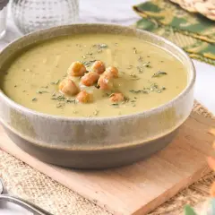 Un tazón de cremosa crema de garbanzos, decorada con garbanzos enteros y hierbas, servida en una tabla de madera.