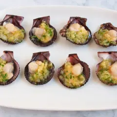 Ocho zamburiñas al horno, listas para disfrutar, con un relleno dorado y perejil picado.