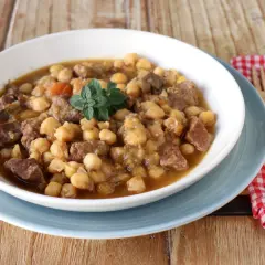 Un plato humeante de garbanzos con carne, perfecto para una receta de garbanzos tradicional. Decorado con una ramita de hierbas frescas.