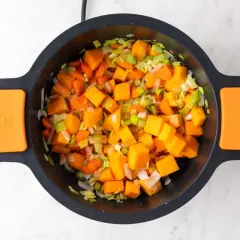 Trozo de calabaza, zanahoria y puerro picados en una olla, listos para hacer una deliciosa crema de verduras.