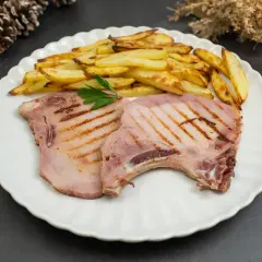 Dos chuletas de sajonia a la parrilla con patatas fritas y perejil en un plato blanco.