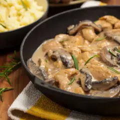 Delicioso pollo con champiñones en salsa cremosa, servido en sartén de hierro fundido, con puré de patatas al lado.