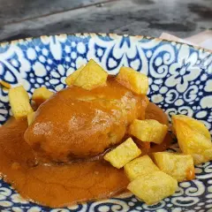 Rollo de bonito en salsa con patatas fritas, servido en un plato azul y blanco.