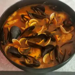 Caldereta de pescado humeante en una olla, repleta de mejillones, almejas y trozos de pescado en una rica salsa roja.