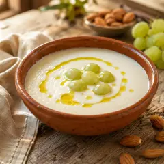 Un refrescante ajo blanco adornado con uvas verdes y un hilo de aceite de oliva, acompañado de almendras.