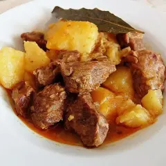 Plato de morcillo de ternera estofado con patatas y una hoja de laurel.