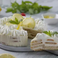 Deliciosa tarta de limón sin horno, con capas de galleta y crema, decorada con merengue, rodajas de limón y menta.
