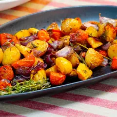 Un plato de verduras al horno, con patatas, zanahorias y cebolla morada, adornado con romero fresco.