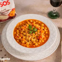 Plato de garbanzos con arroz, pimientos y zanahoria, decorado con perejil. Acompañado de una copa de vino tinto y una bolsa de arroz SOS.