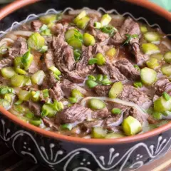 Un reconfortante plato de ternera guisada con trozos de carne tierna, fideos y espárragos verdes, servido en un cuenco rústico.