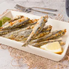 Boquerones crujientes en freidora de aire, servidos en plato blanco con limón y perejil.